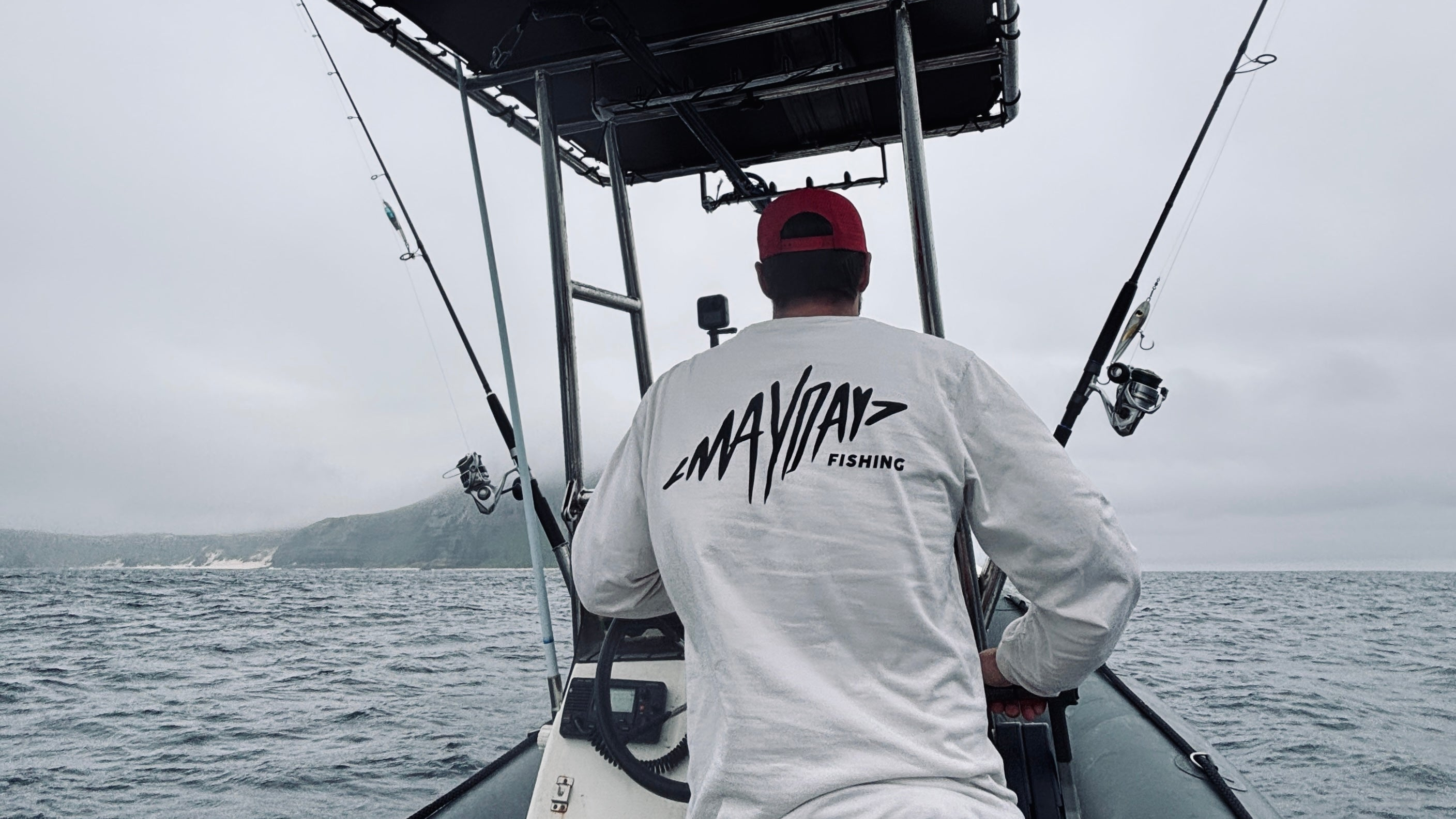 Person on a boat wearing a 'Mayday Fishing' shirt with a cloudy sky and water background.