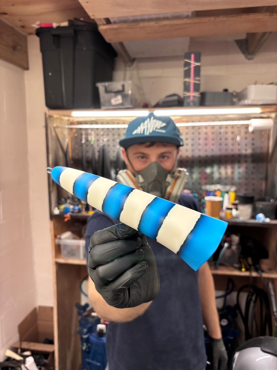 Person holding a blue and white saltwater lure popper in a workshop setting